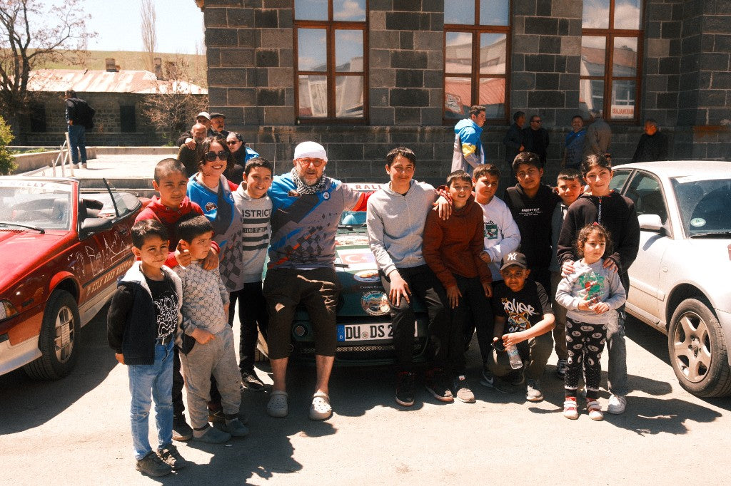 Rally driver with local children next to the rally cars